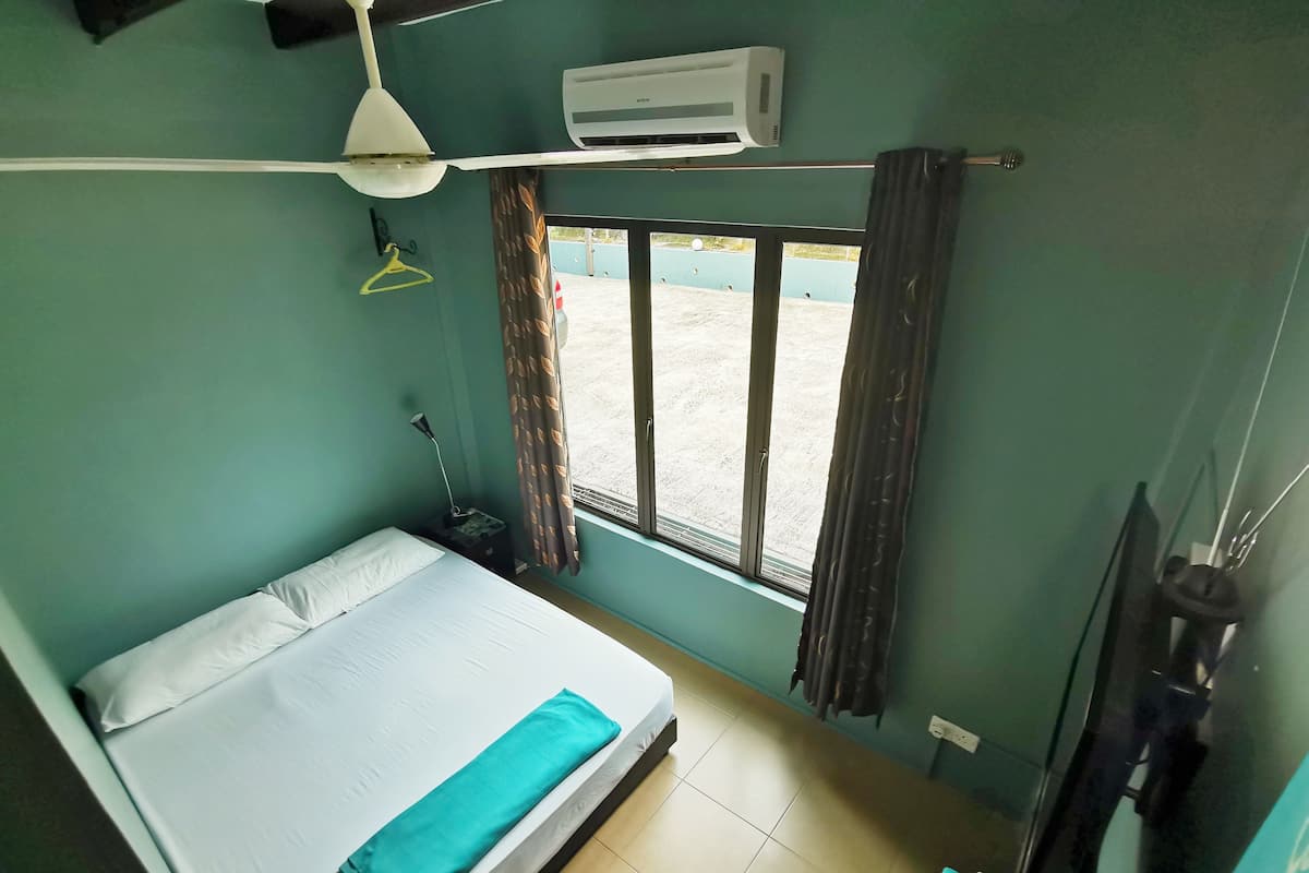 Una habitación con cama, aire acondicionado, ventana con cortinas y televisión.