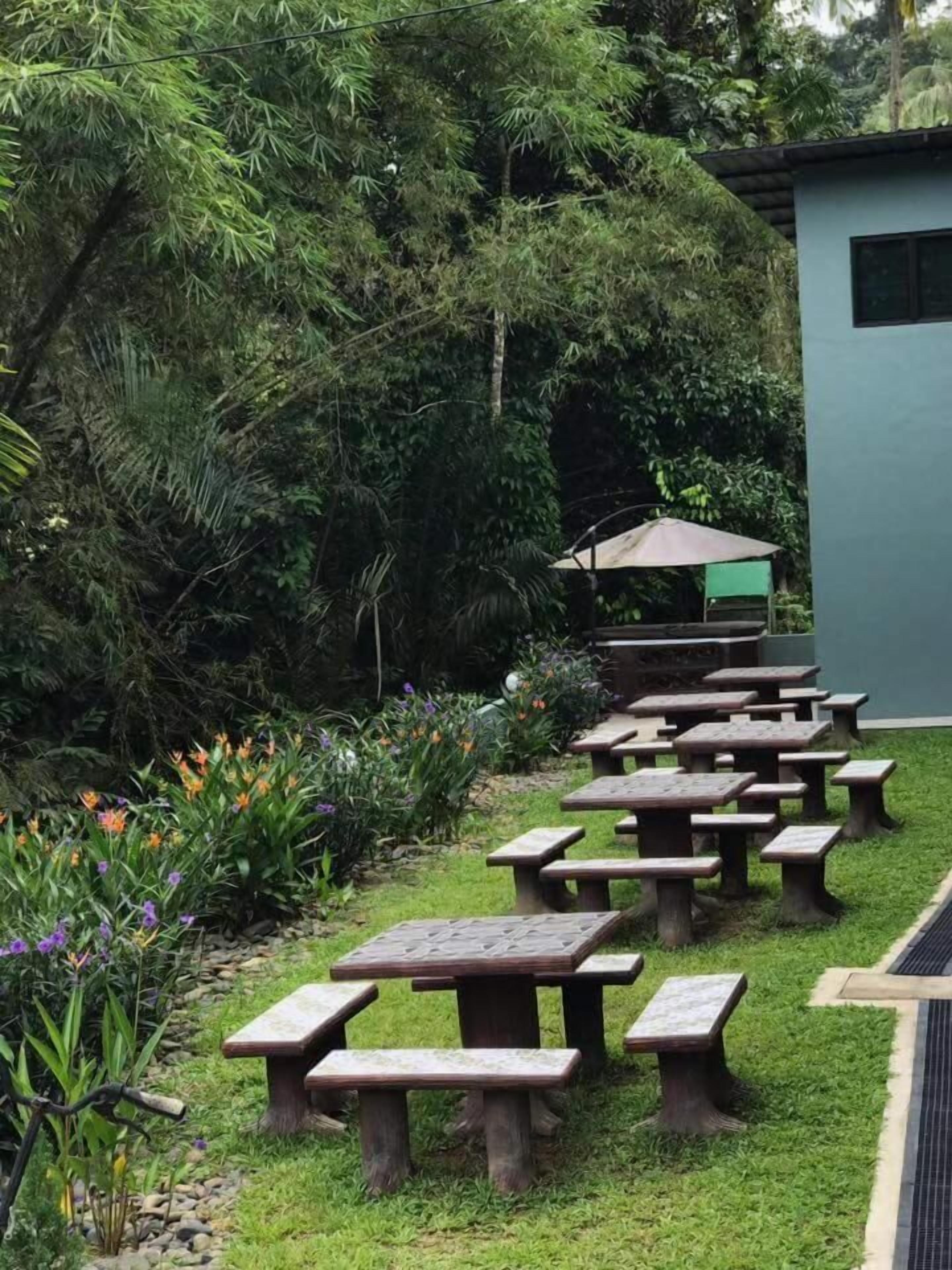 A garden with multiple wooden picnic tables arranged in rows, surrounded by lush greenery and flowering plants.