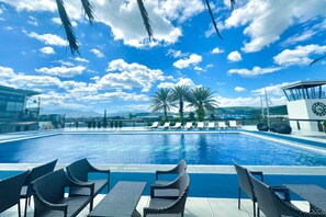 A swimming pool with lounge chairs and palm trees, surrounded by a clear blue sky. - Le Charmé Suites (Olongapo)