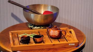 A round wooden table with a metal bowl, a wooden spoon, a teapot, and two cups.