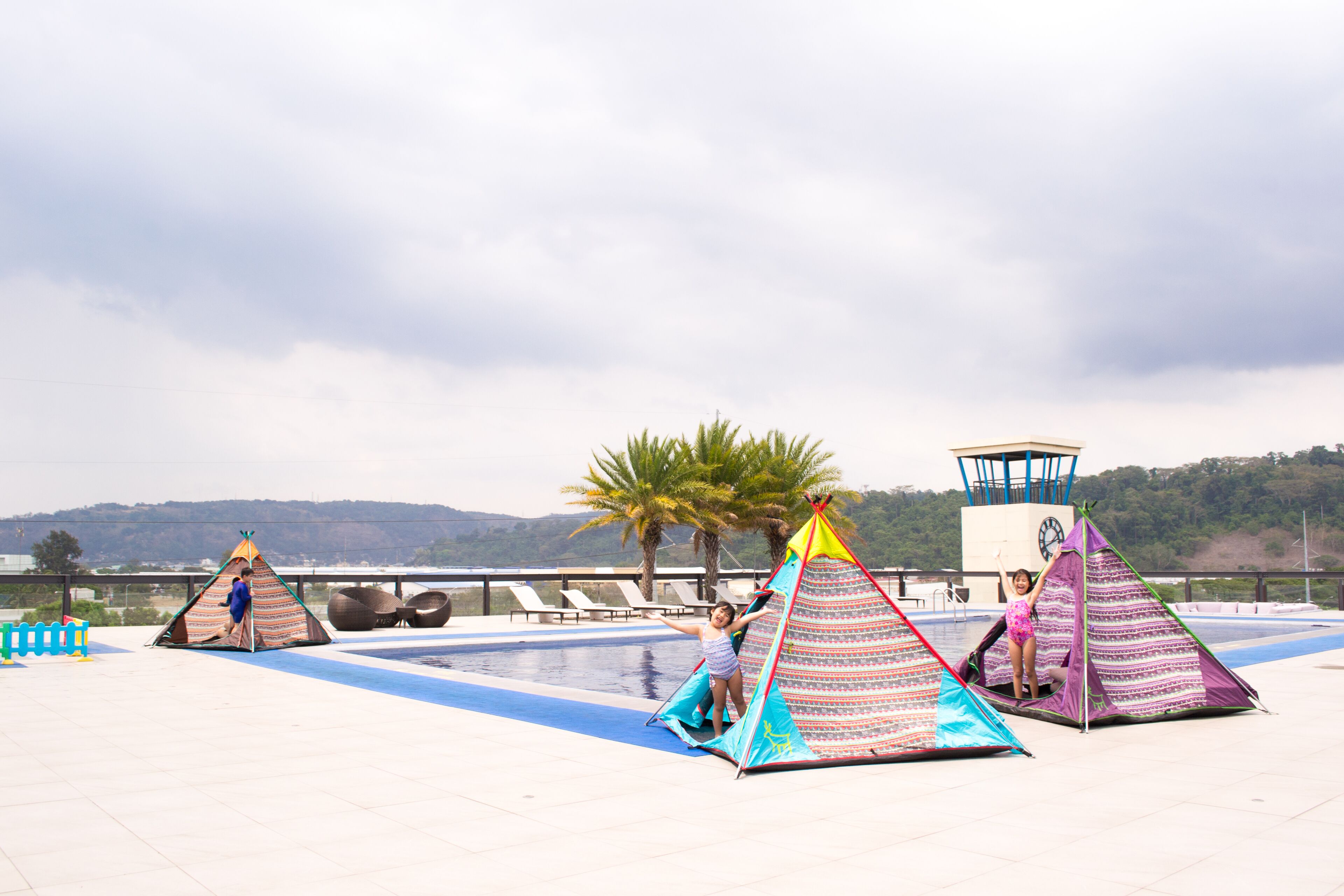 A rooftop pool area with three colorful tents and a lifeguard tower.