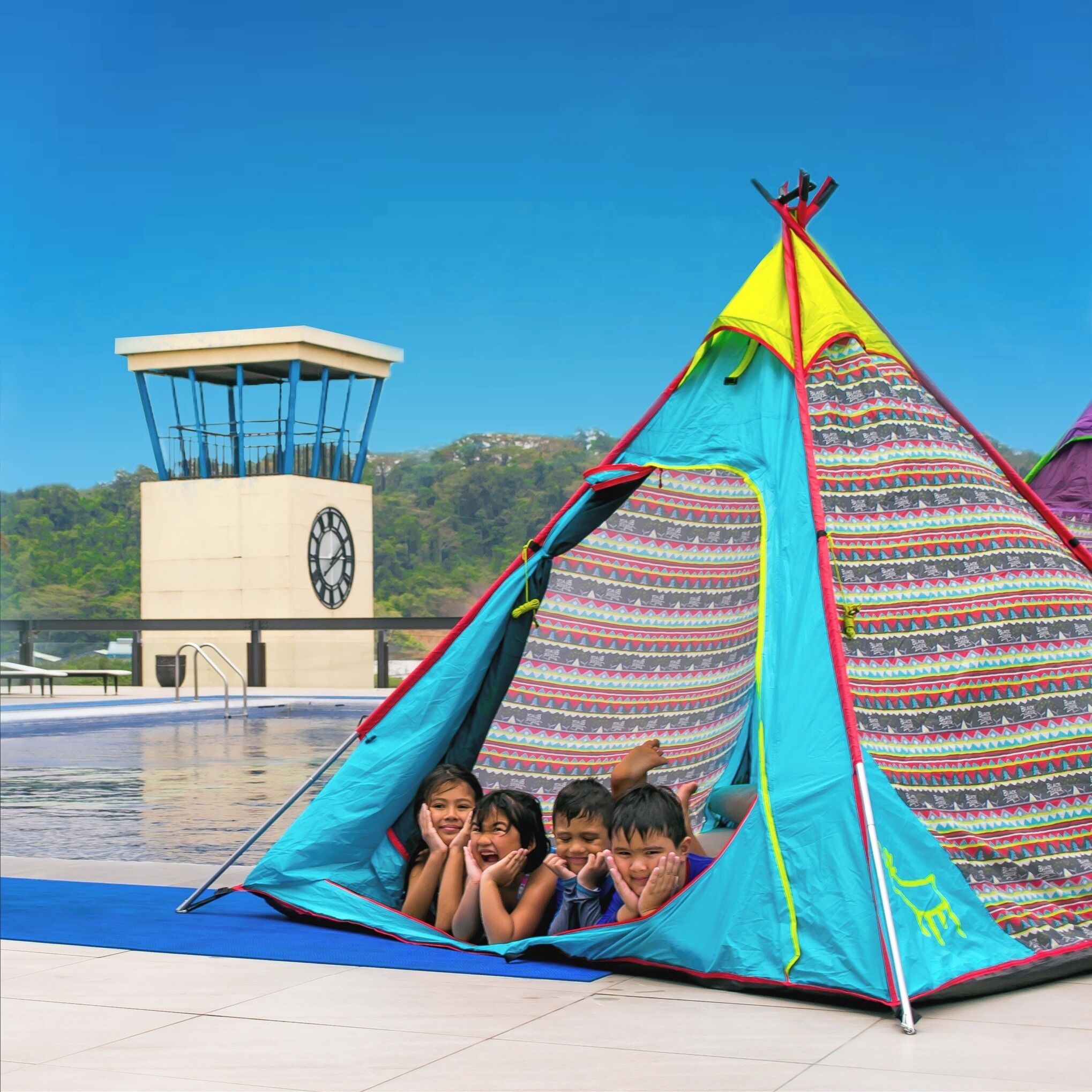 A colorful tent near a swimming pool with a clock tower in the background.