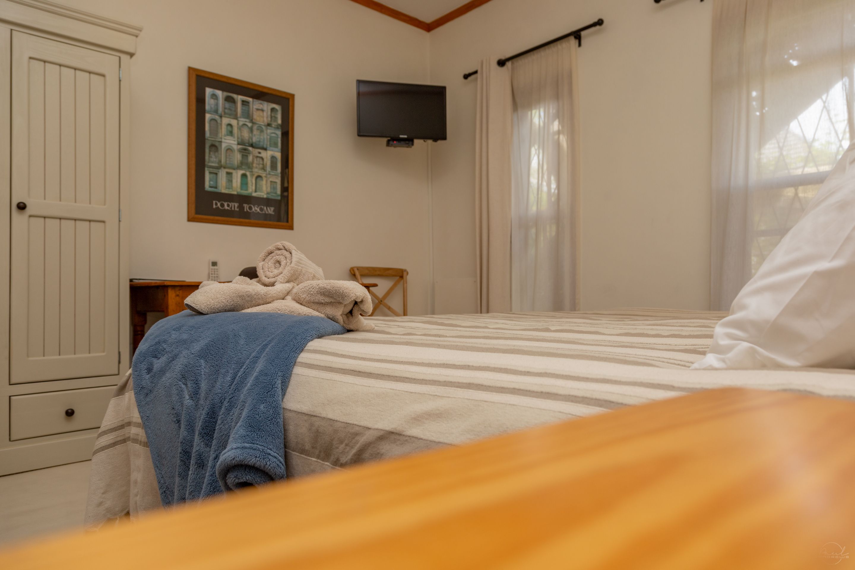 Ein Schlafzimmer mit Bett, Wandfernseher, Fenster mit Vorhängen und Tür.