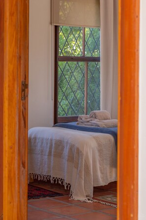 A bedroom with a bed, a window with a view of greenery, and a wooden door. - 10 Alexander B&B (Stellenbosch)