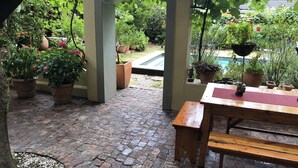 A covered patio area with a brick floor, wooden bench, and potted plants. - 10 Alexander B&B (Stellenbosch)