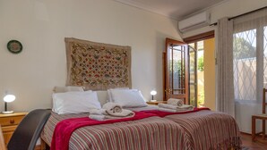 A neatly made bed with a striped bedspread, two bedside lamps, and a decorative tapestry on the wall. - 10 Alexander B&B (Stellenbosch)