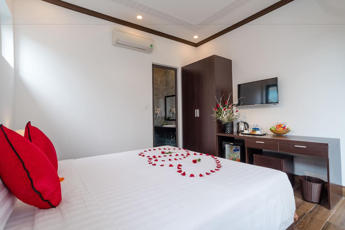 A hotel room with a bed, a desk, a TV, and a bathroom visible through an open door.