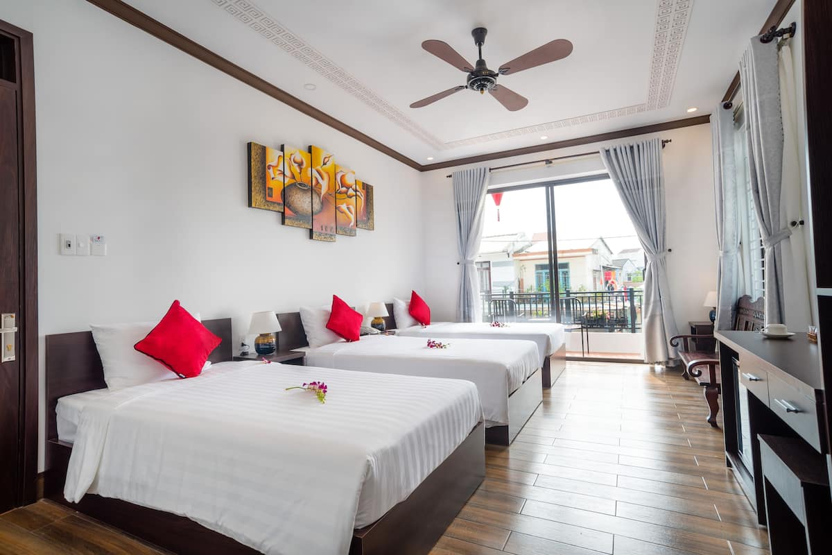 A hotel room with two beds, a ceiling fan, artwork on the wall, and a view of the outside.