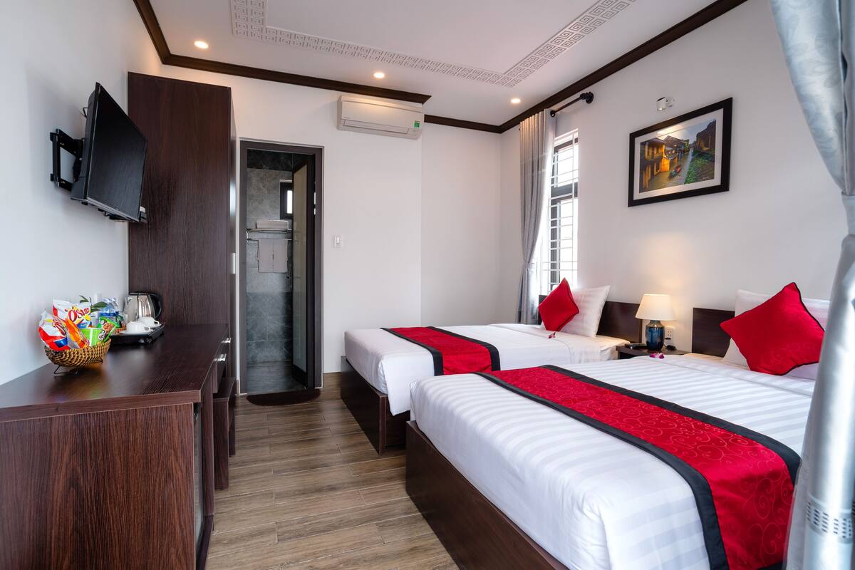 A hotel room with two beds, a desk, a TV, and a window with curtains.