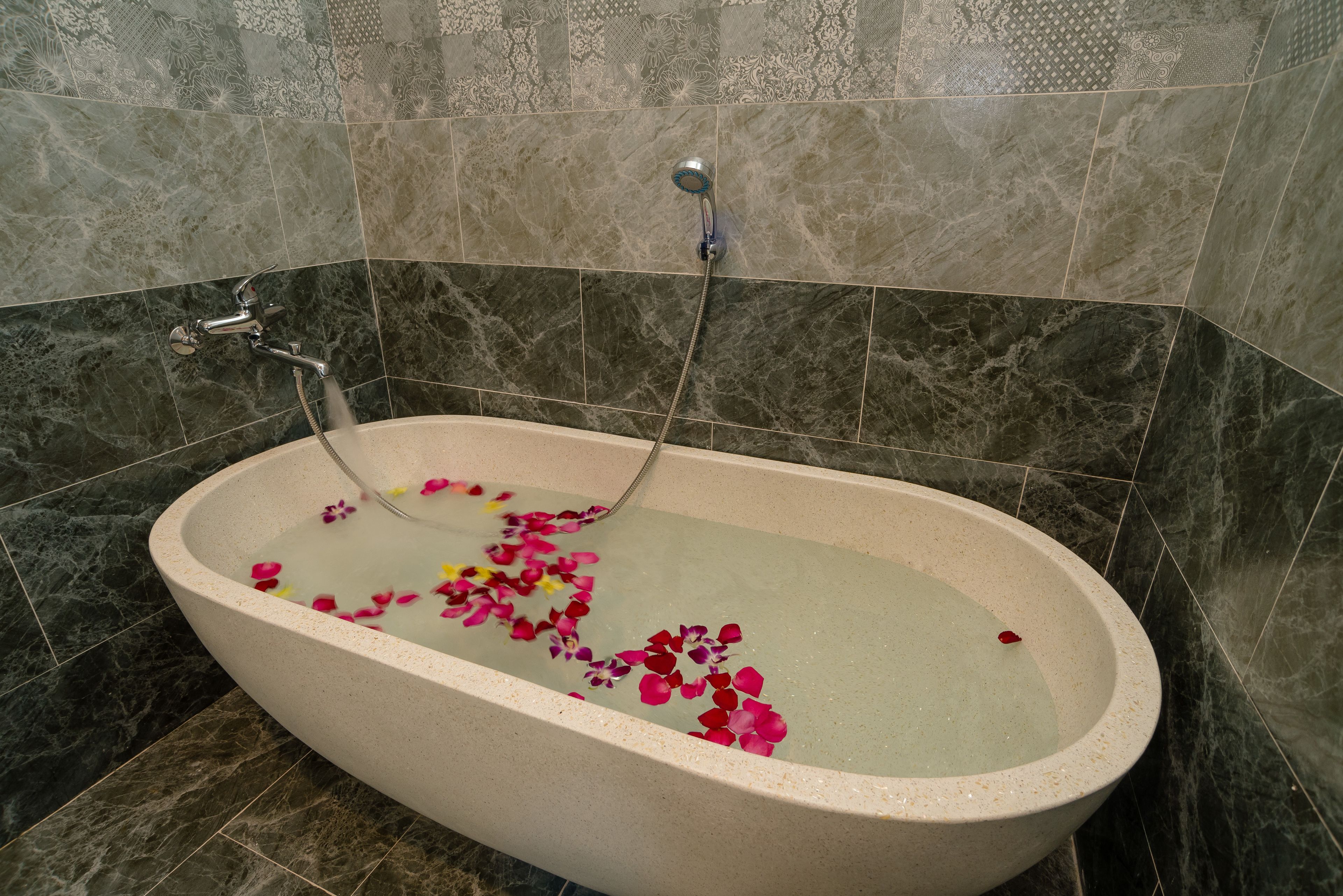 A bathtub with water and rose petals, set against a tiled wall.