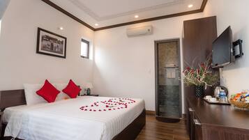 A hotel room with a neatly made bed, a television, a bathroom, and a wooden desk with a vase of flowers.