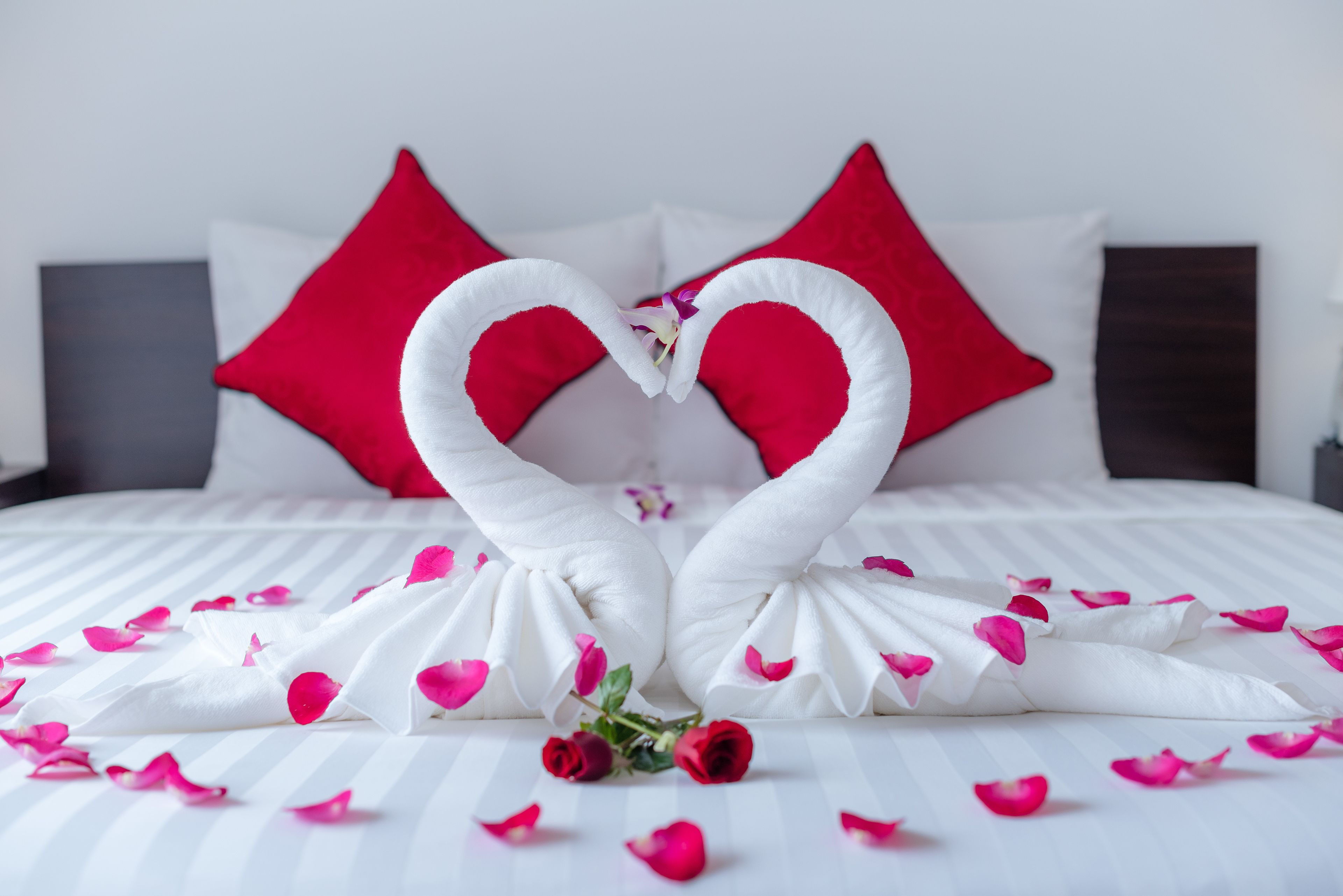 Ein Bett mit weißer Bettwäsche, roten Kissen und einer herzförmigen Handtuchanordnung.