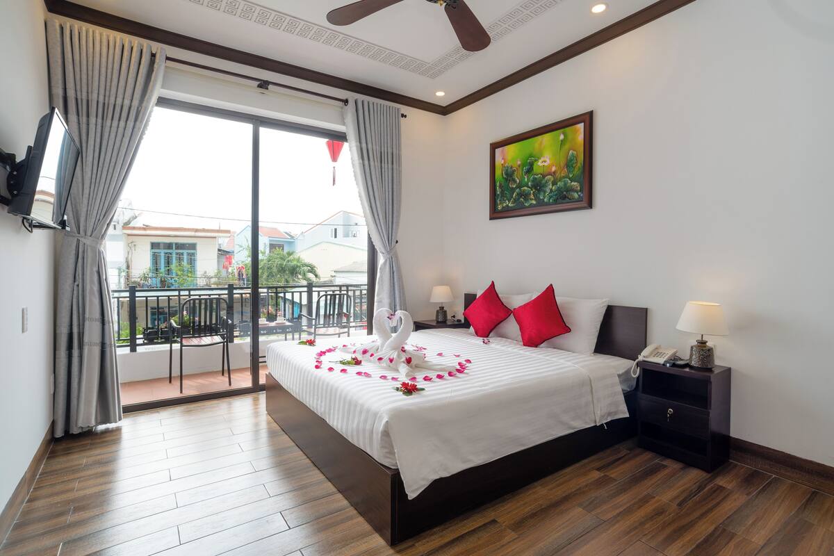 A hotel room with a large bed, a balcony, a painting, and a nightstand with a lamp.