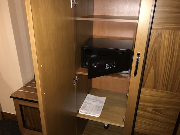 A wooden cabinet with a black electronic device on a shelf, a small table with papers, and a door handle. - Hotel Colosseo Tirana (Tirana)