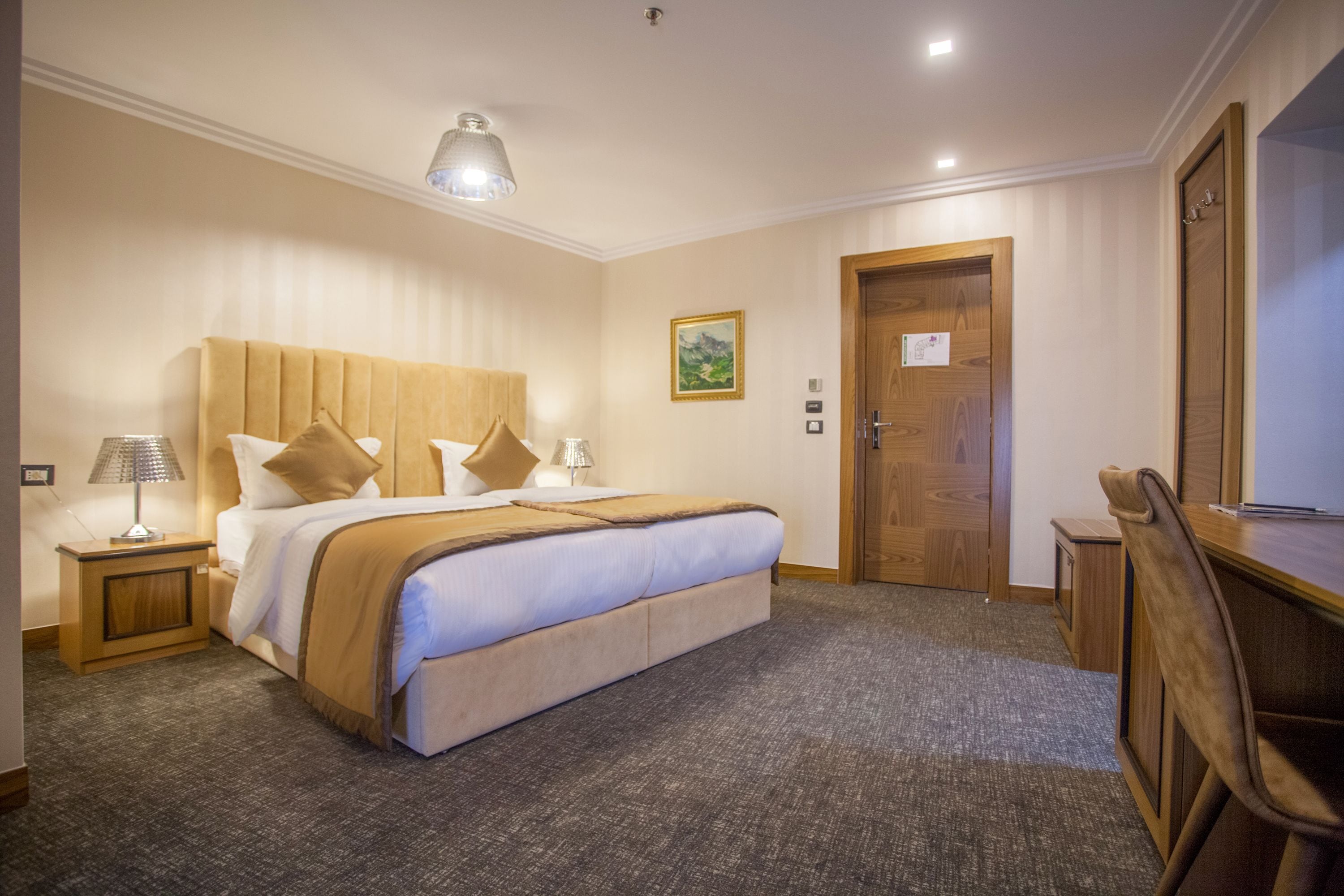 Une chambre d’hôtel avec un grand lit, une tête de lit en bois, un bureau et une chaise.