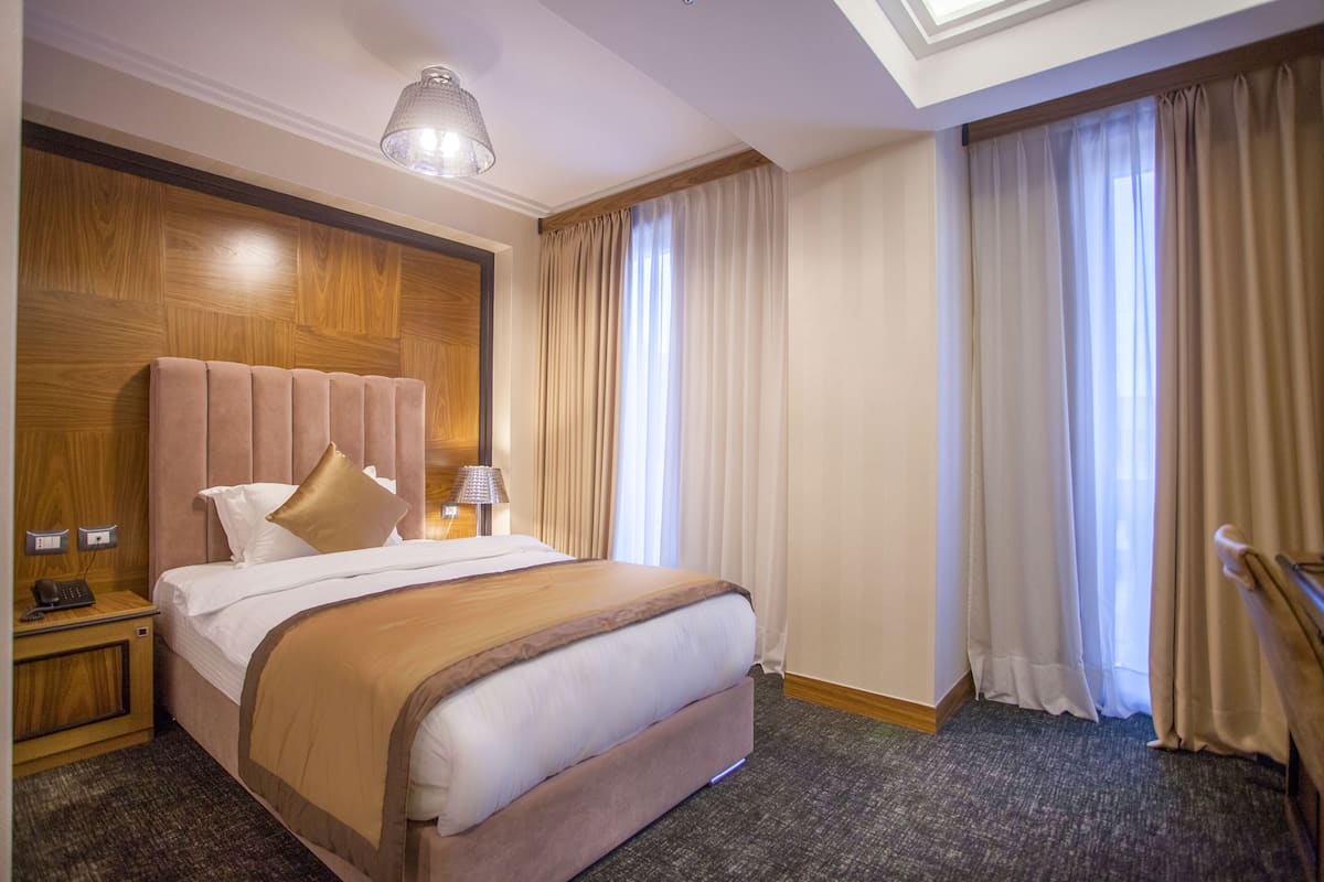 A hotel room with a large bed, wooden headboard, and a nightstand with a lamp.
