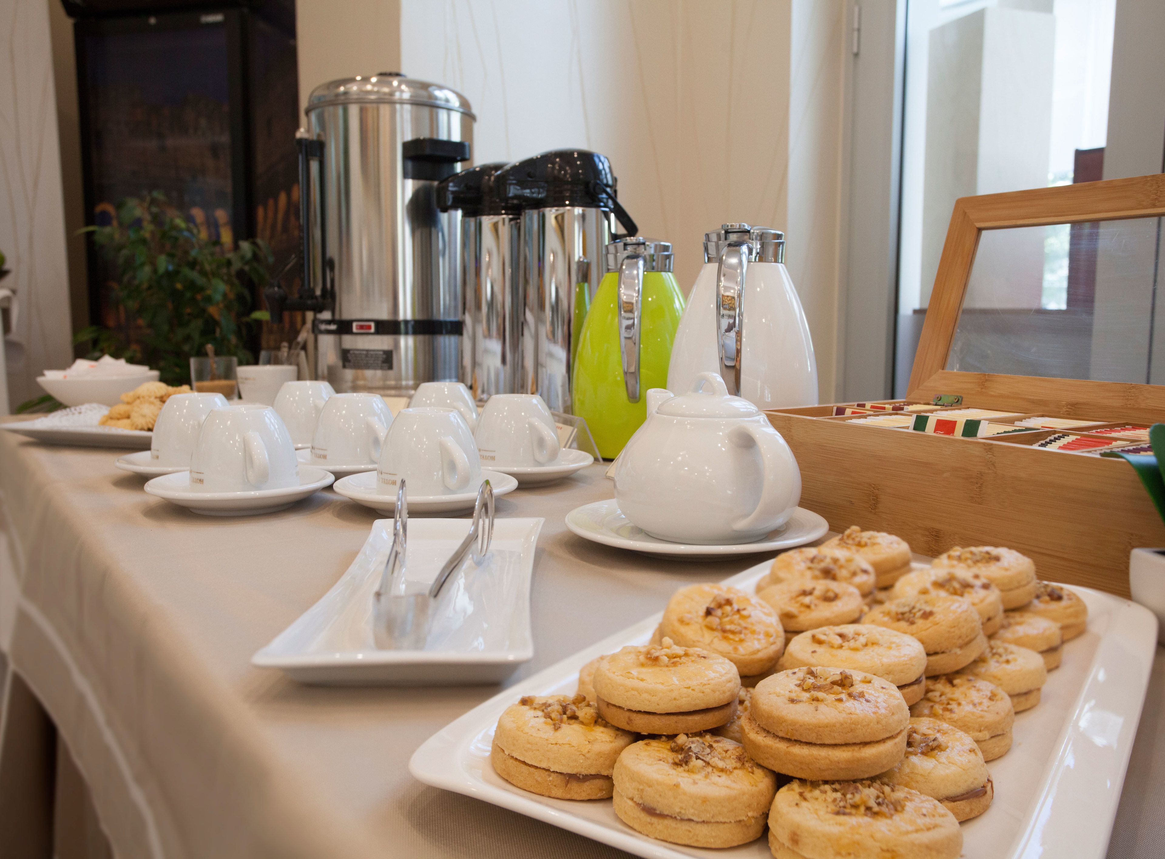 Un bufé de desayuno con tazas blancas, una tetera y un plato de galletas.