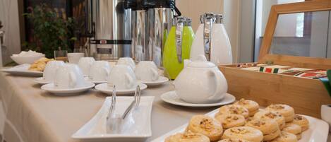 Un bufé de desayuno con tazas blancas, una tetera y un plato de galletas.