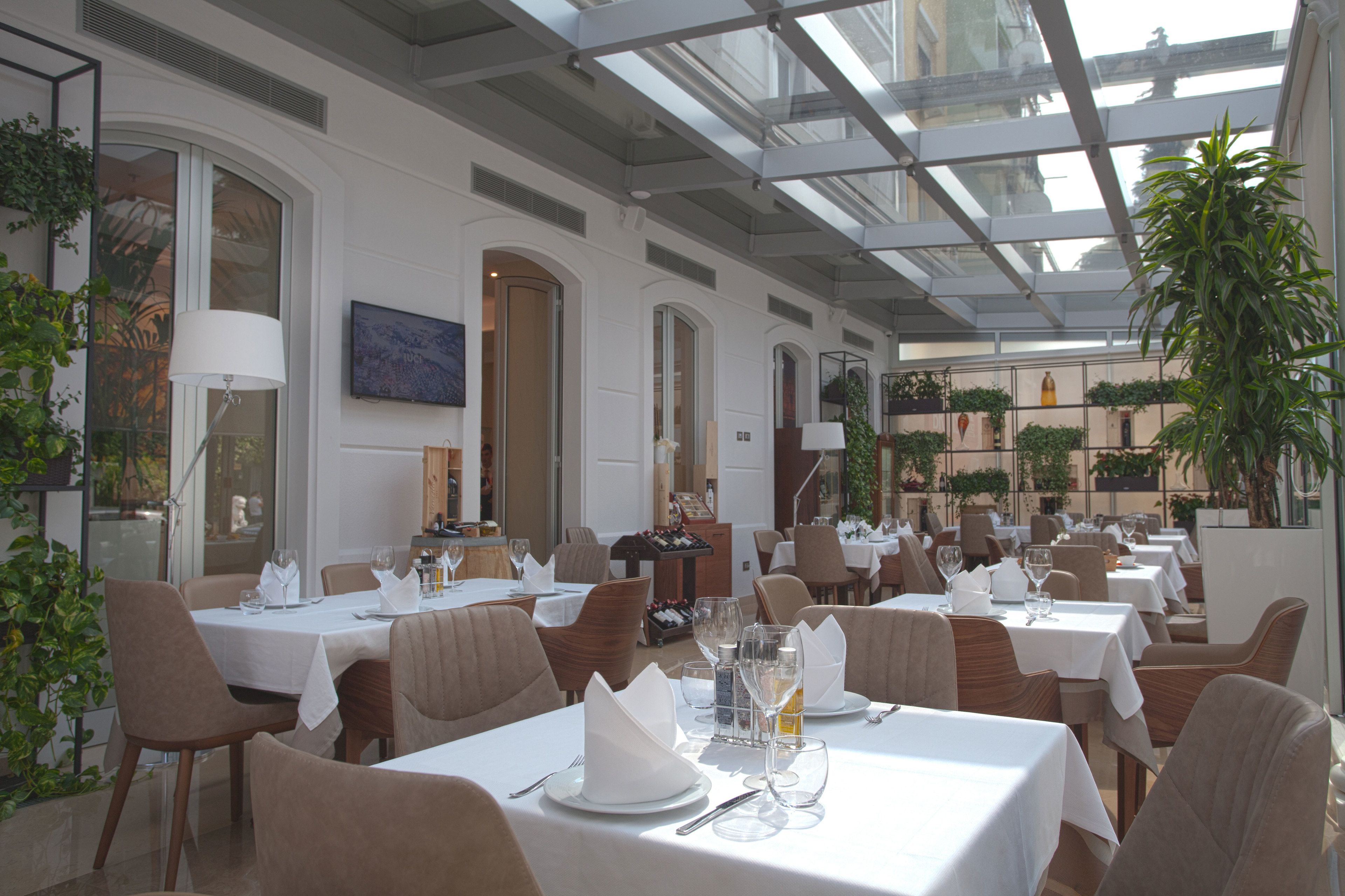 Een restaurant met meerdere tafels voor diners, met een glazen plafond en kamerplanten.