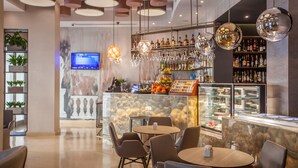 Un área de bar moderna con mesas y sillas redondas, una pantalla de televisión y una variedad de botellas y vasos en estanterías.