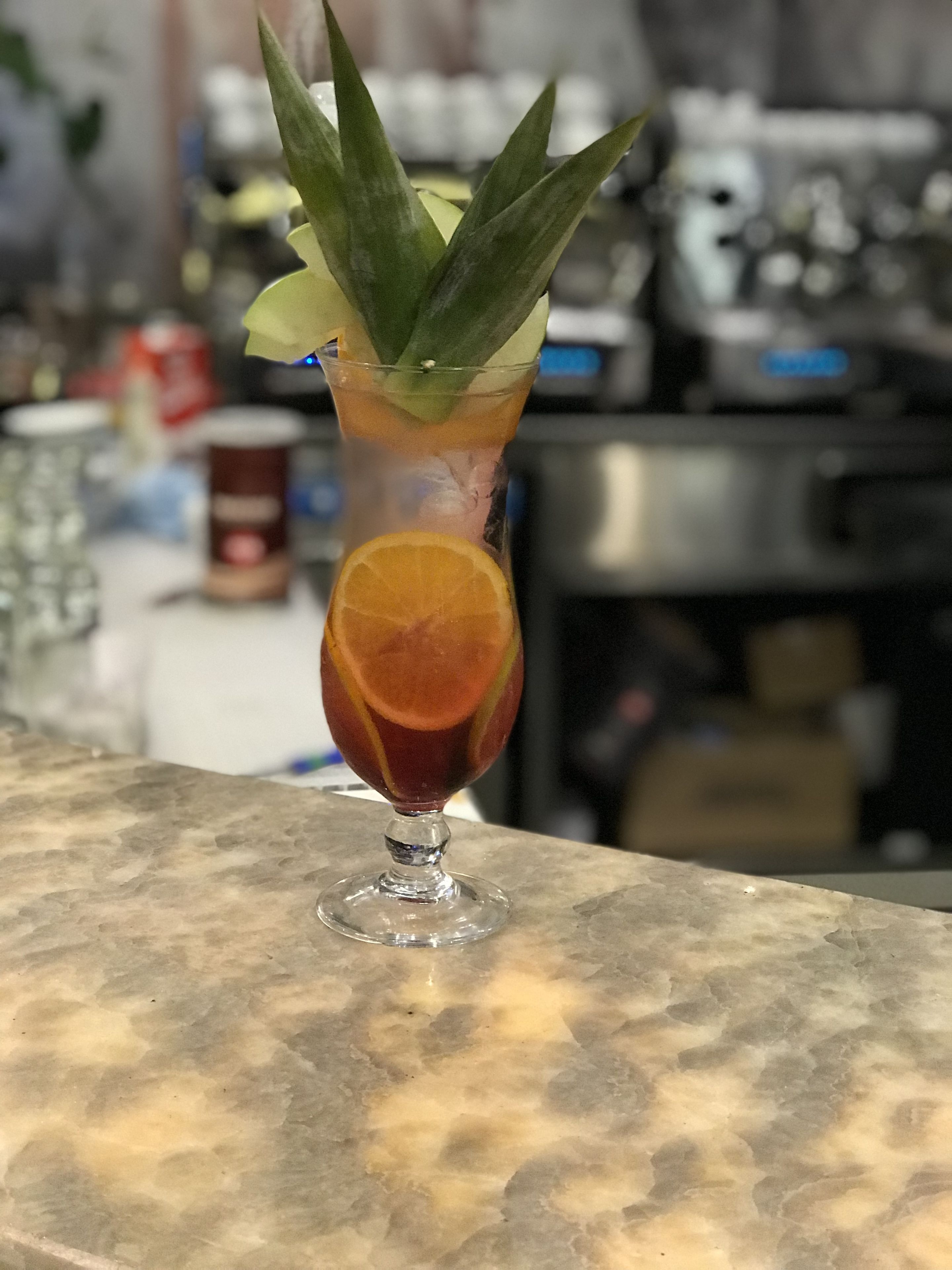Un vaso de cóctel con una rodaja de naranja y una hoja de menta sobre una encimera de mármol.
