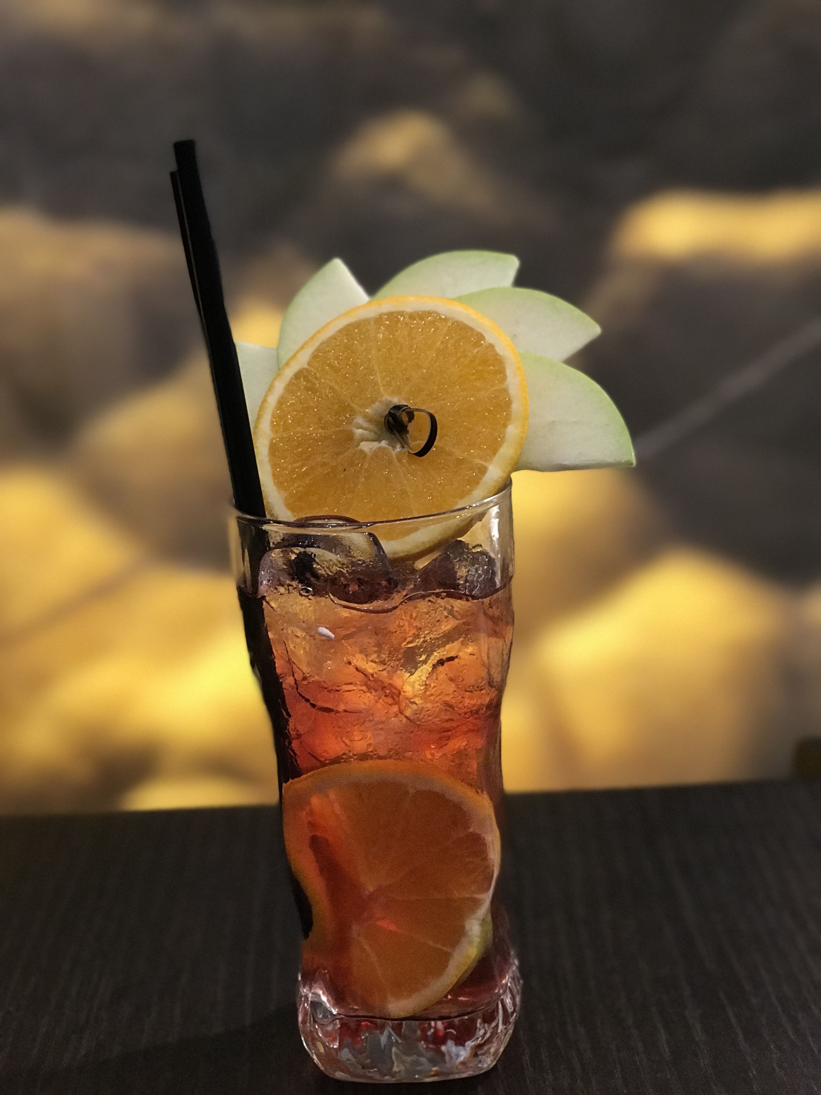 Un grand verre contenant une boisson, des glaçons et une tranche d’orange posée sur le bord.