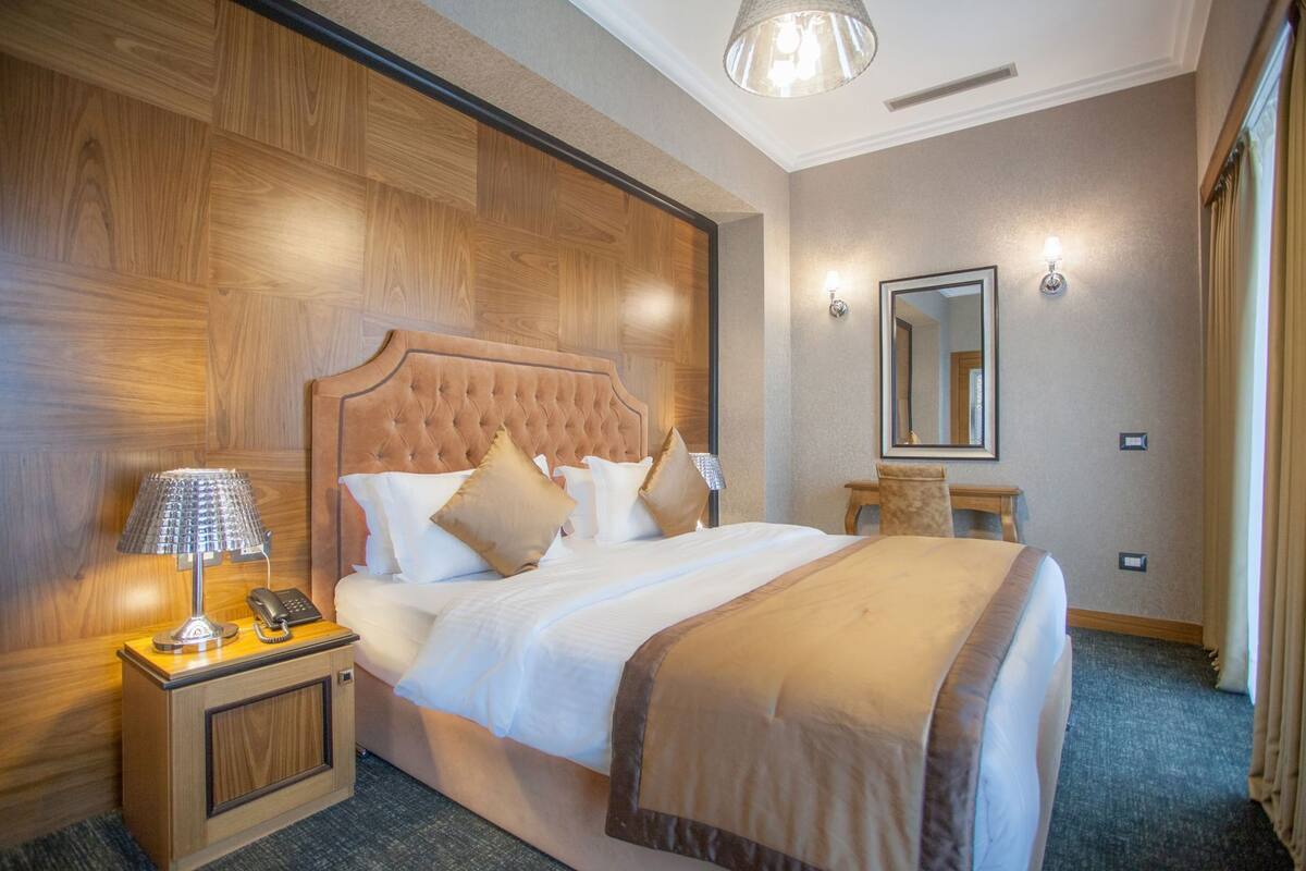 A hotel room with a large bed, a bedside lamp, a telephone, a small table, and a mirror.