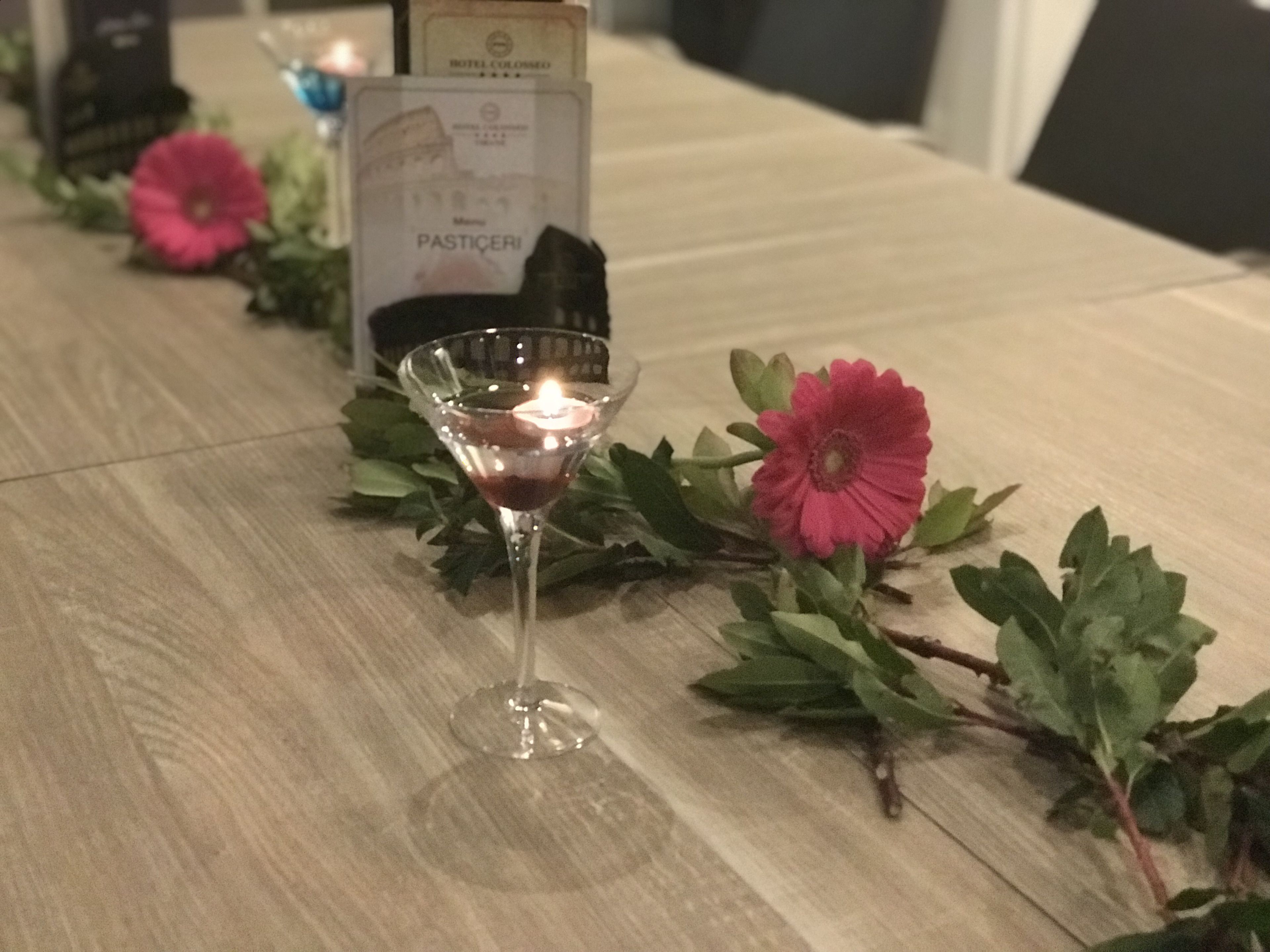 Une table avec un verre à martini, une bougie allumée et une fleur rose.