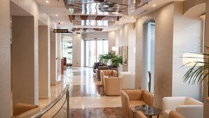 Un vestíbulo de hotel con piso de mármol, asientos de cuero, barandilla de vidrio y techo con diseño geométrico.