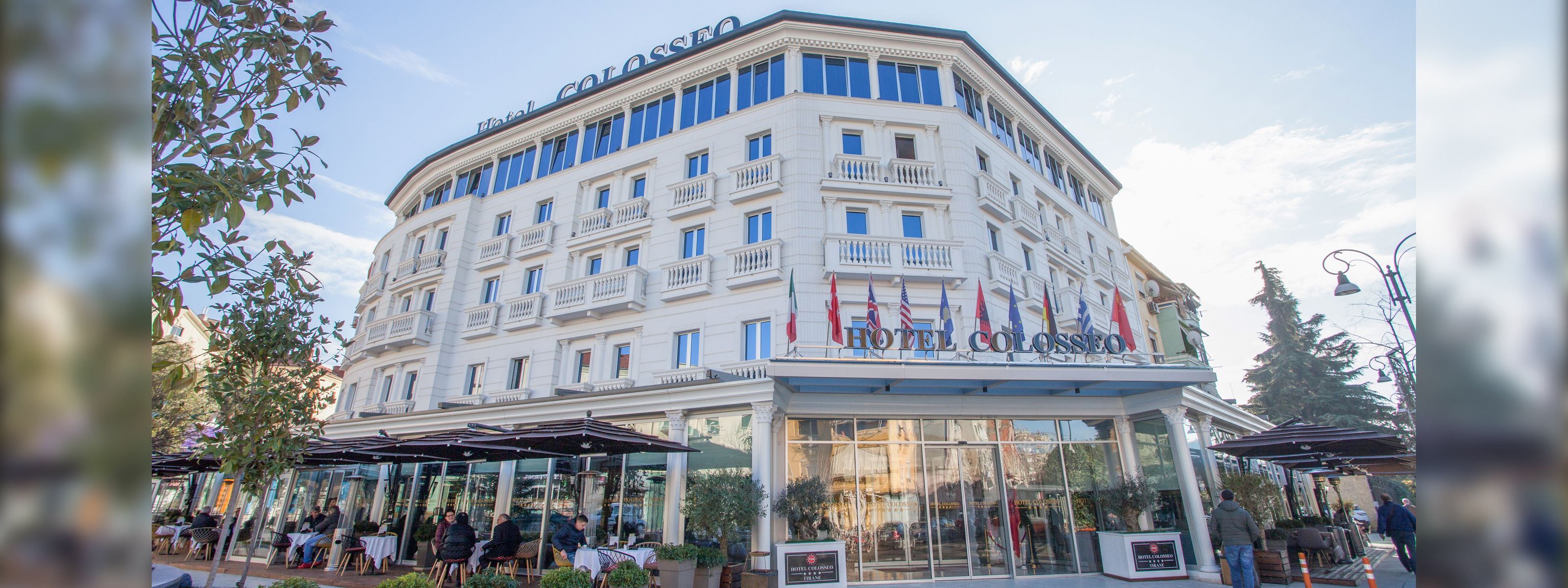 A hotel with a classic European architectural style, featuring a prominent balcony on the second floor, large glass windows, and a welcoming entrance with a sign.