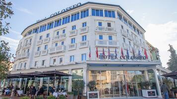 A hotel with a classic European architectural style, featuring a prominent balcony on the second floor, large glass windows, and a welcoming entrance with a sign.