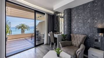 A modern living room with a large sliding glass door leading to a balcony, a tufted armchair, a white coffee table, and a desk with chairs.