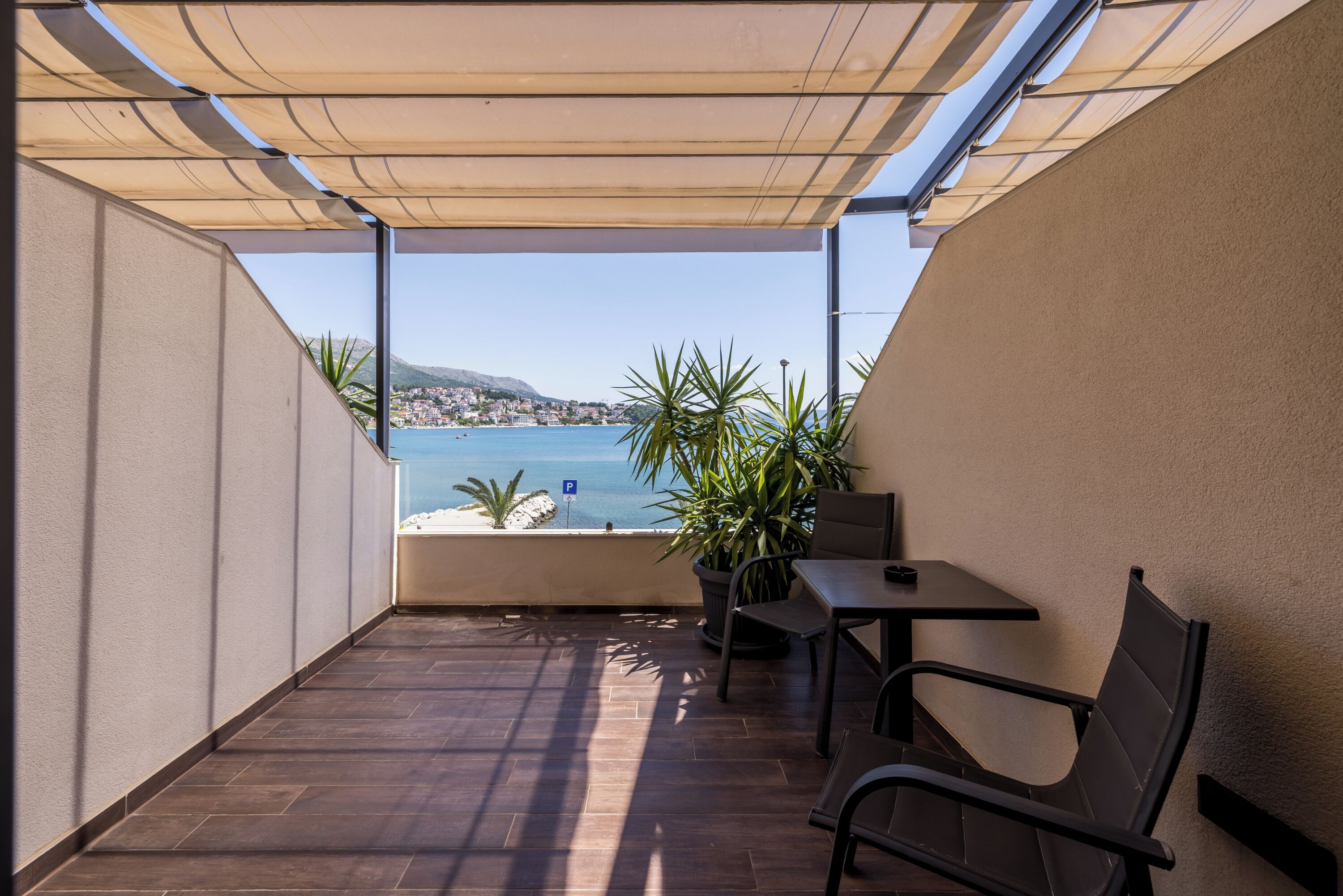 A balcony with a view of the sea, a table, chairs, and potted plants.