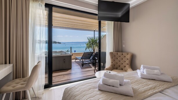 A hotel room with a bed, a chair, a TV, and a view of the sea.