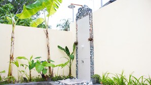 A small, enclosed outdoor shower area with a tiled floor, surrounded by plants and a decorative stone wall.
