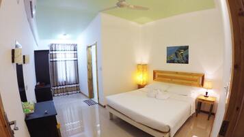 A hotel room with a bed, bedside lamps, a ceiling fan, a painting, and a bathroom visible through an open door.