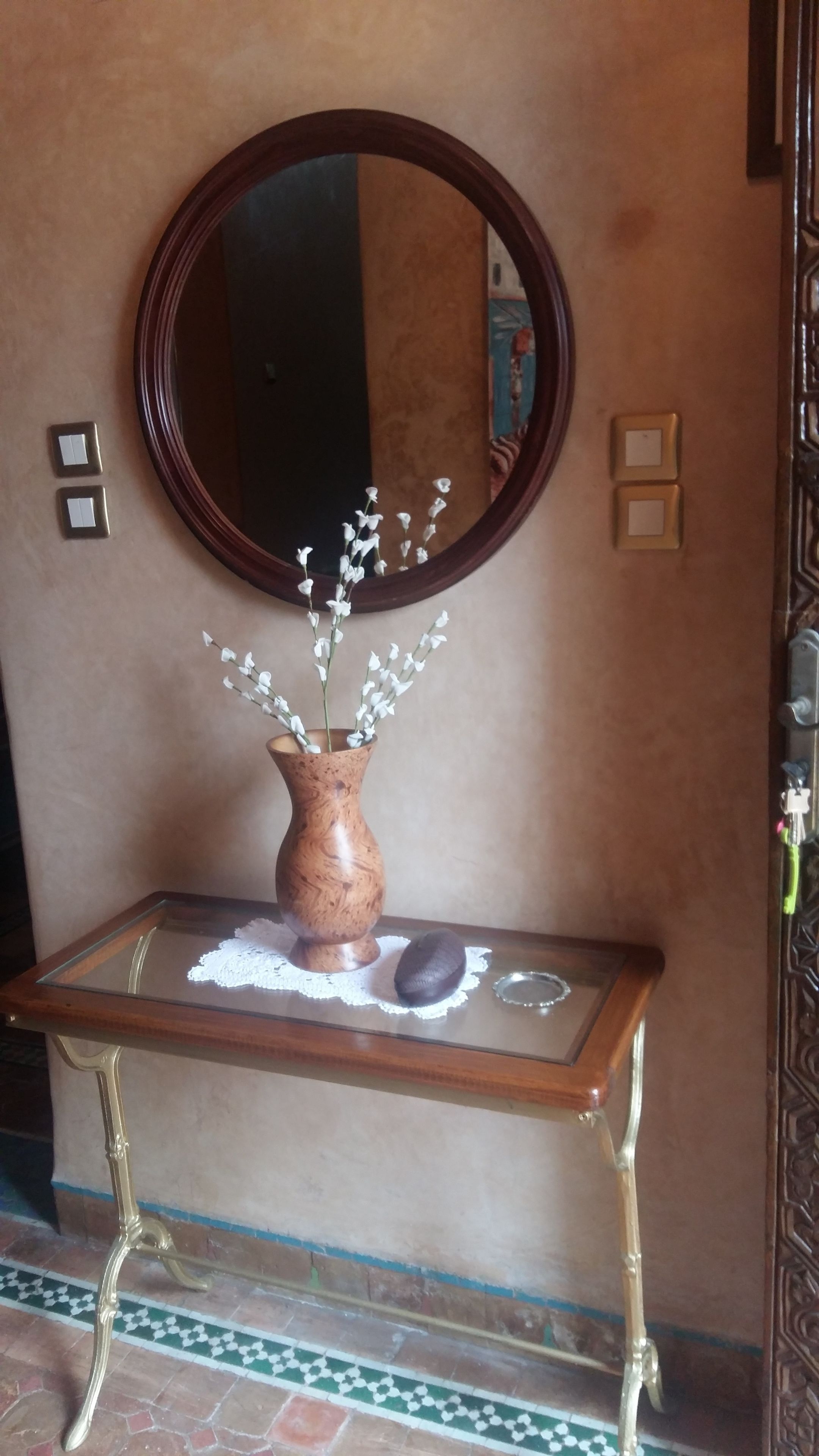 Uma pequena mesa com um vaso de flores brancas, um tampo de vidro e um objeto decorativo.