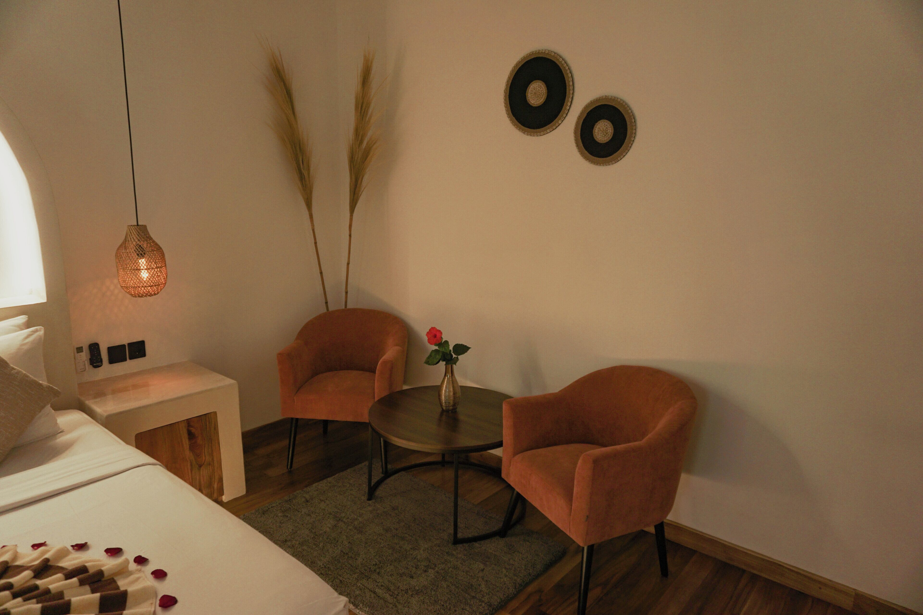 A room with a bed, two chairs, a small table with a vase, and two wall-mounted circular decorations.