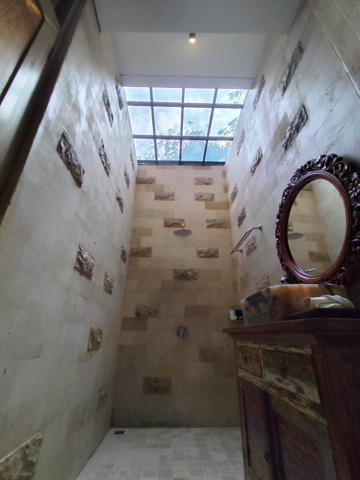 A narrow bathroom with a skylight, a shower, and a vanity with a mirror.
