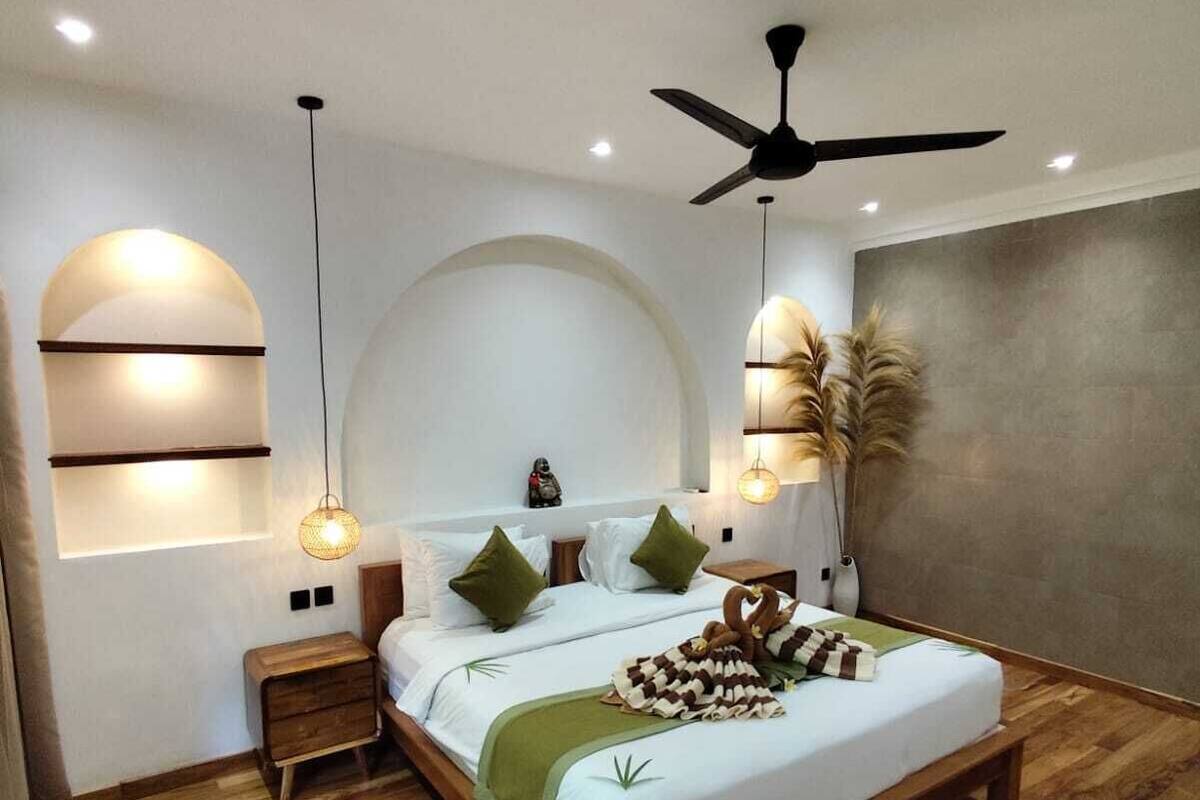 A modern bedroom with a wooden bed, two bedside tables, a ceiling fan, and a large arched window.