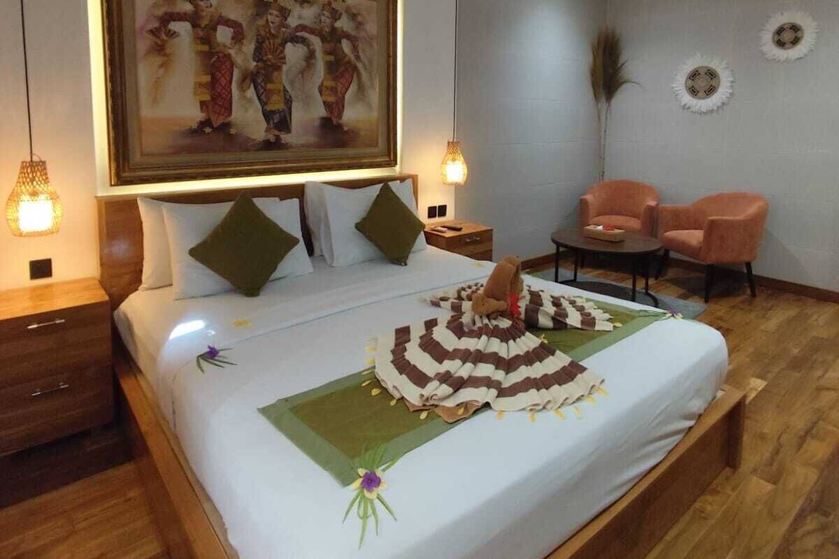 A bedroom with a large bed, a ceiling fan, a painting on the wall, and a small table with chairs.