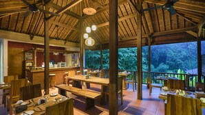 Un comedor espacioso con mesas y bancos de madera, una zona de bar y ventanas amplias que ofrecen vistas del bosque circundante.