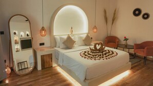 Un dormitorio moderno con una cama grande, un tocador con espejo, dos sillas y una mesita con un florero.