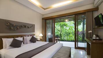 A hotel room with a large bed, a television, a desk, and a view of greenery through the sliding doors.
