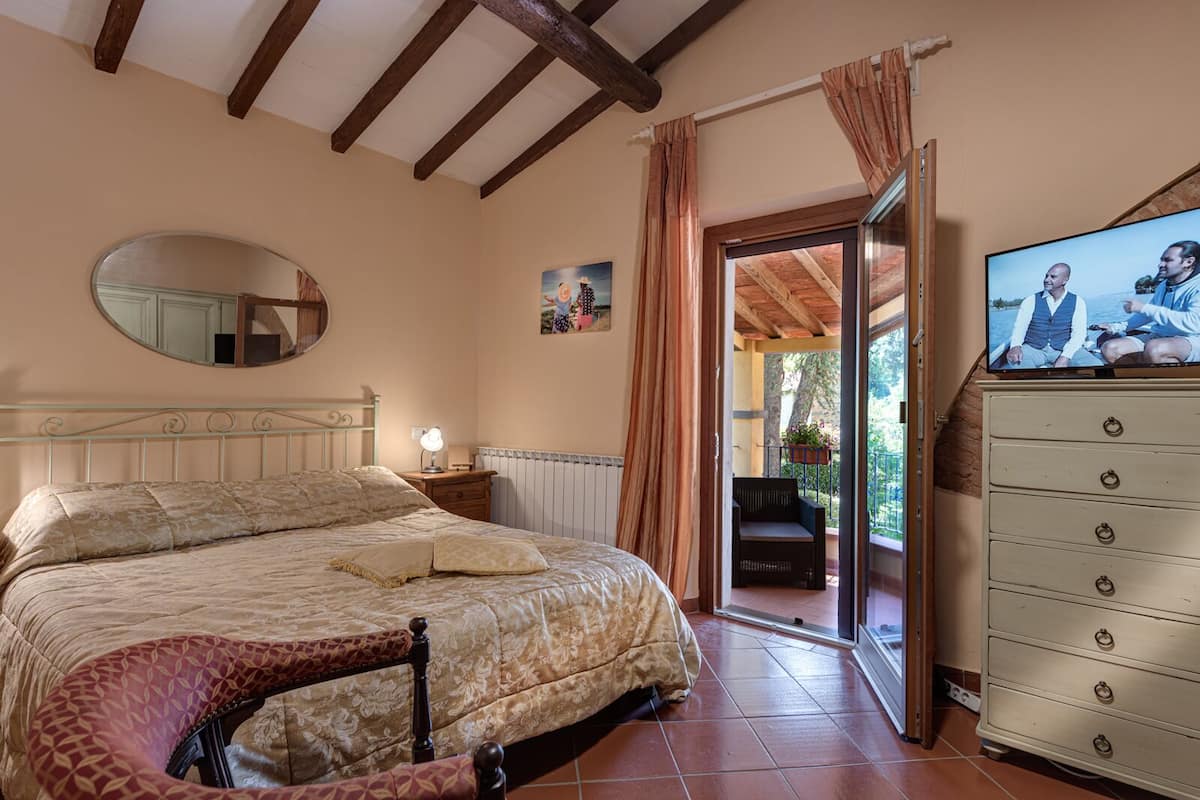 A bedroom with a bed, a dresser, a mirror, a TV, and a balcony with a chair.