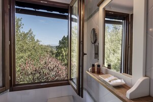 Un baño con un ventanal grande, un espejo y artículos de aseo en el mostrador.