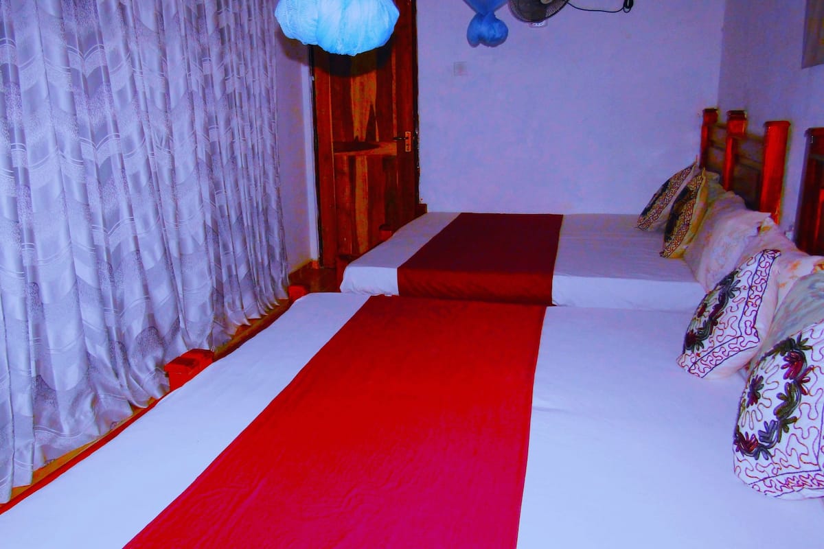 A hotel room with a bed, a red and white striped bed runner, a white curtain, and a blue hanging light fixture.