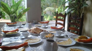 A breakfast table set with plates of toast, fruit, and coffee cups, surrounded by chairs and potted plants. - Pura Sanda Villa (Inamaluwa)