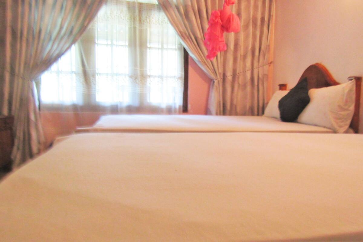 A hotel room with two beds, a window with curtains, and a wall-mounted telephone.