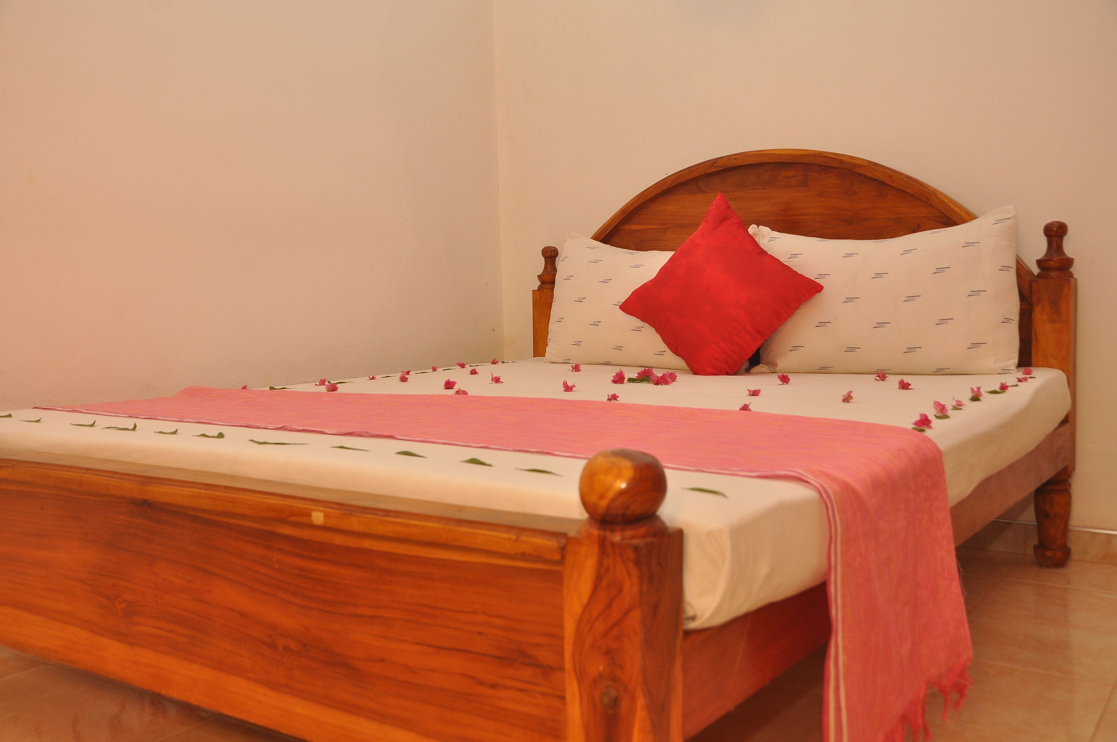A wooden bed with a white mattress, a red pillow, and a pink blanket.